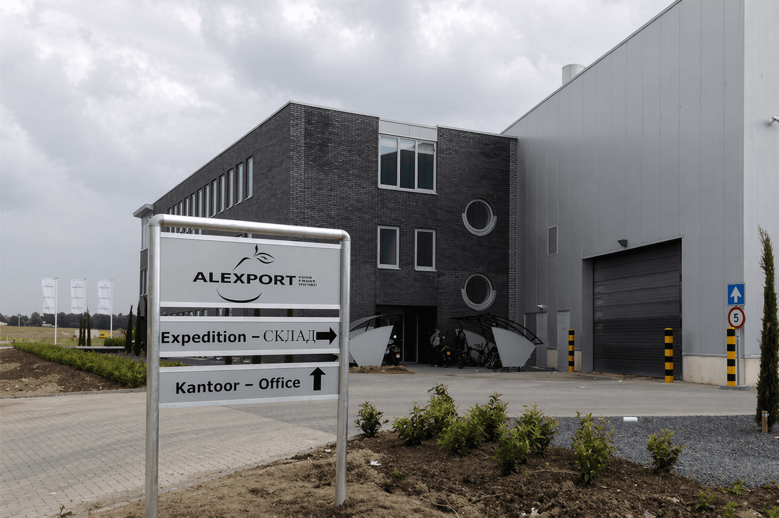 Vrijstaand wayfinding-bord met ALEXPORT-logo, richtingsaanduidingen voor expeditie en kantoor, geplaatst voor een modern bedrijfsgebouw met laadpoort.
