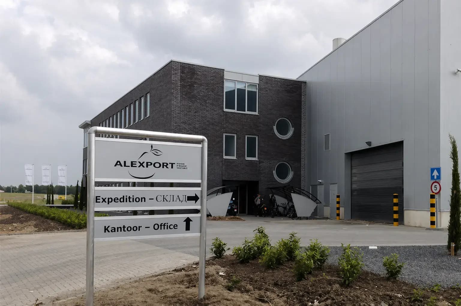 Vrijstaand wayfinding-bord met ALEXPORT-logo, richtingsaanduidingen voor expeditie en kantoor, geplaatst voor een modern bedrijfsgebouw met laadpoort.