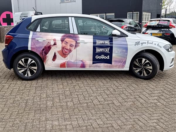 Witte en blauwe personenauto met full-colour voertuigbelettering voor diervoeding, voorzien van grote fotoprint op de zijkant en geparkeerd op een bedrijventerrein.