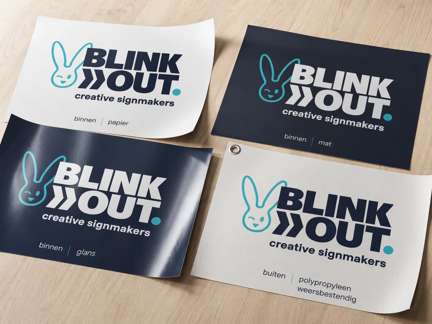 Vier BLINK OUT creative signmakers-printstalen op hout, met het logo op verschillende materialen en afwerkingen voor binnen en buiten, waaronder papier, mat, satijn en weerbestendig polypropyleen.