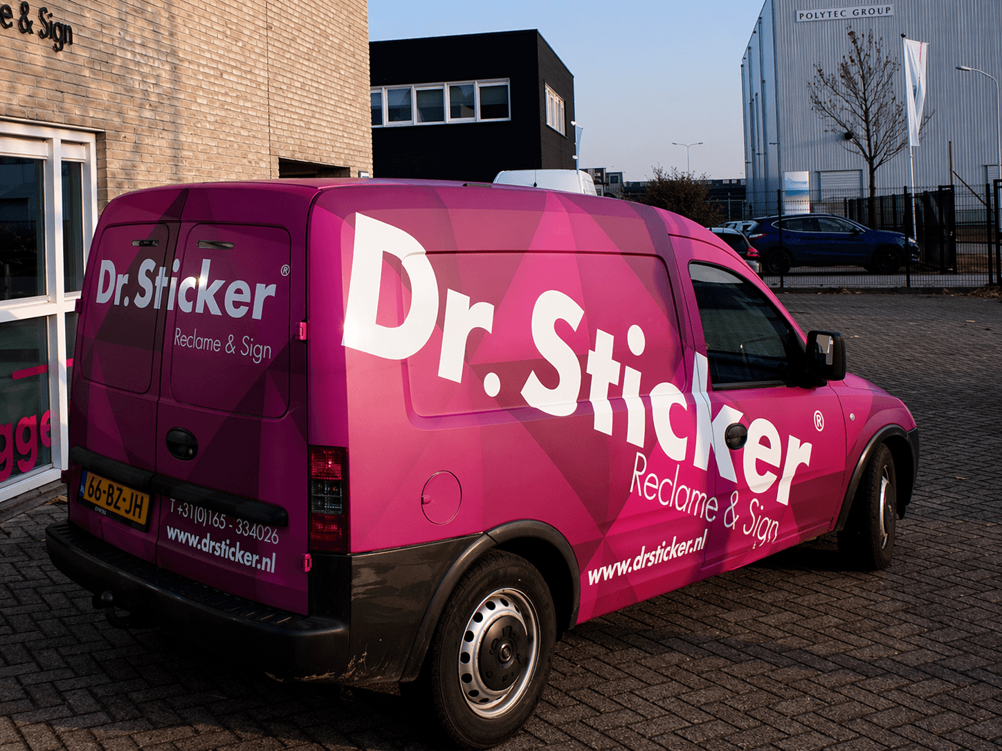 Felroze bedrijfsbus met volledige voertuigbelettering en carwrap van Dr.Sticker Reclame & Sign, voorzien van grote witte logoletters en geometrisch patroon, geparkeerd op een bedrijventerrein voor een bedrijfspand.