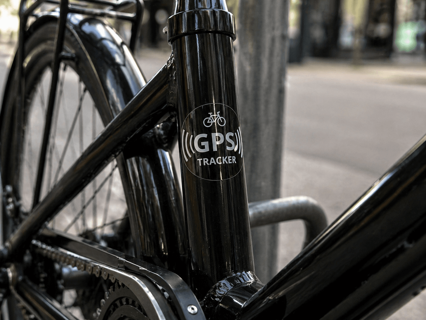 Transparante GPS tracker sticker met wit pictogram en tekst op het zwarte frame van een fiets, toegepast als beveiligingslabel tegen diefstal.