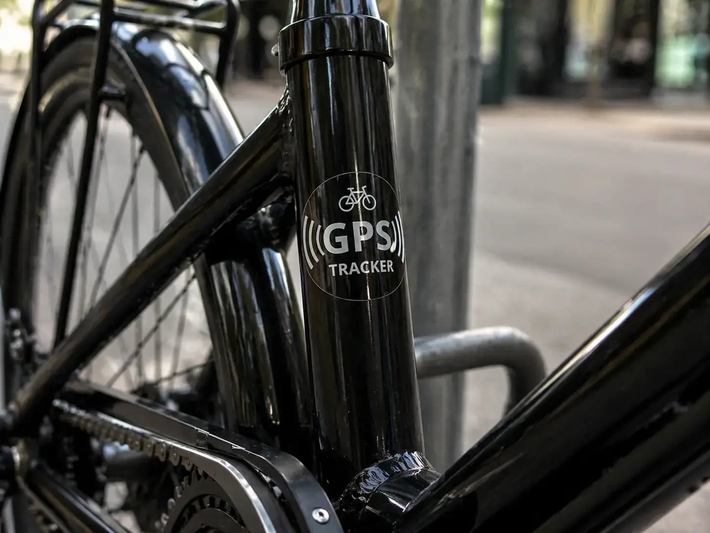 Transparante GPS tracker sticker met wit pictogram en tekst op het zwarte frame van een fiets, toegepast als beveiligingslabel tegen diefstal.