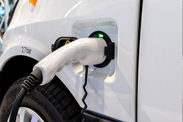 Close-up van een laadkabel in het laadpunt van een witte elektrische bedrijfswagen, met groene laadindicator en detail van de voertuigzijde.