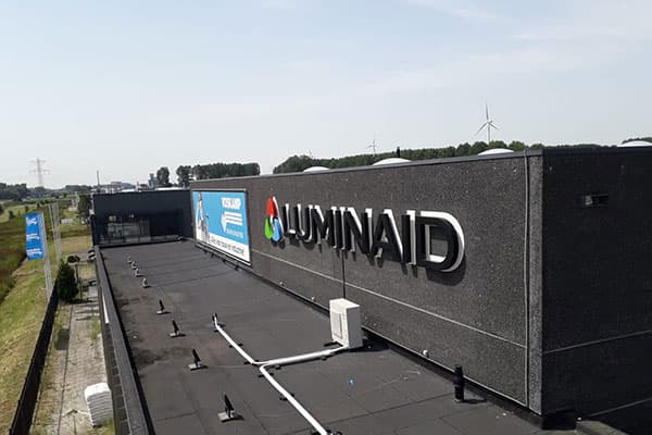 Donkere gevel van een bedrijfspand met gevelreclame van Luminaid, bestaande uit een full-colour logo en witte 3D doosletters langs een plat dak.