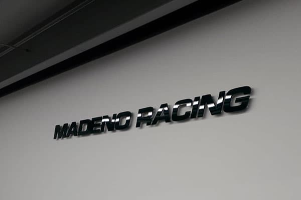 Witte binnenwand met glanzende zwarte 3D letters "MADENO RACING" als strakke interieurbelettering.
