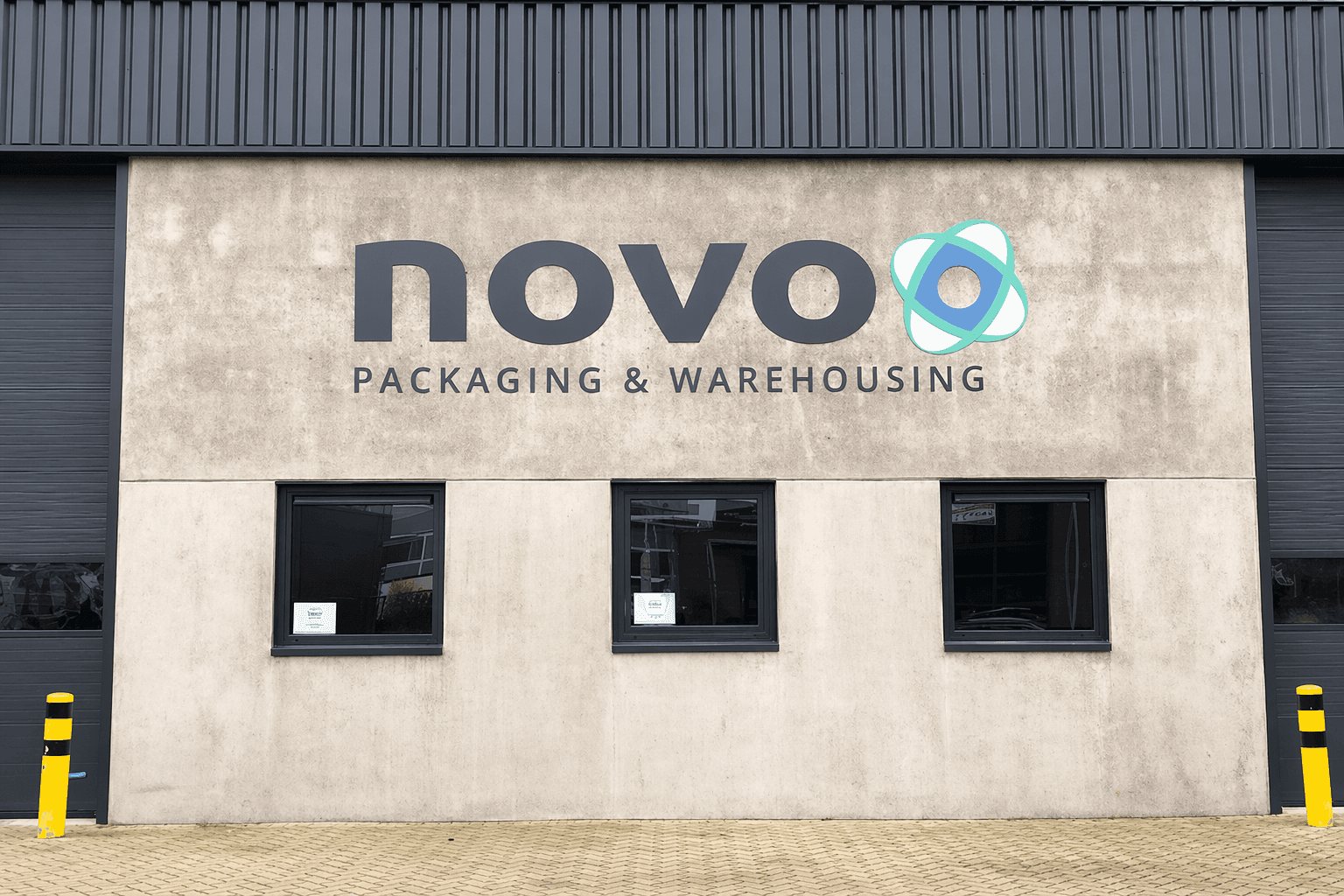 Bedrijfsgevel met groot novo-logo en bedrijfsbelettering Packaging & Warehousing op een betonnen gevel boven drie ramen.