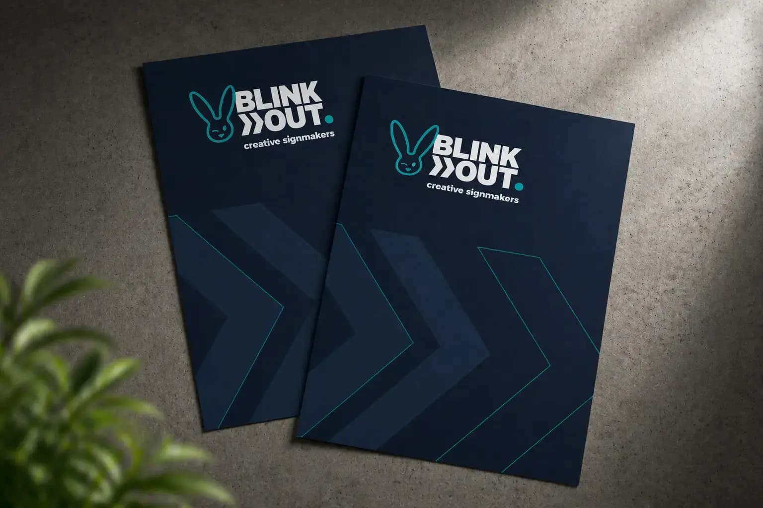 Twee donkerblauwe Posters met BLINK OUT creative signmakers-logo en grafische pijlmotieven, gepresenteerd op een betonnen ondergrond.