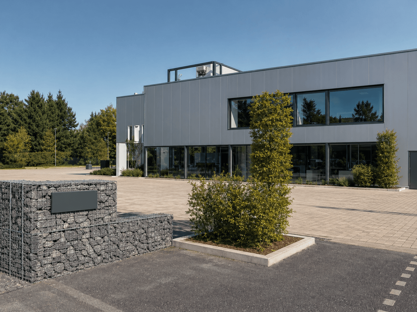 Modern bedrijfspand met grijze gevelbekleding, grote glaspartijen en een rechthoekig gevelbord op een schanskorf bij de entree.