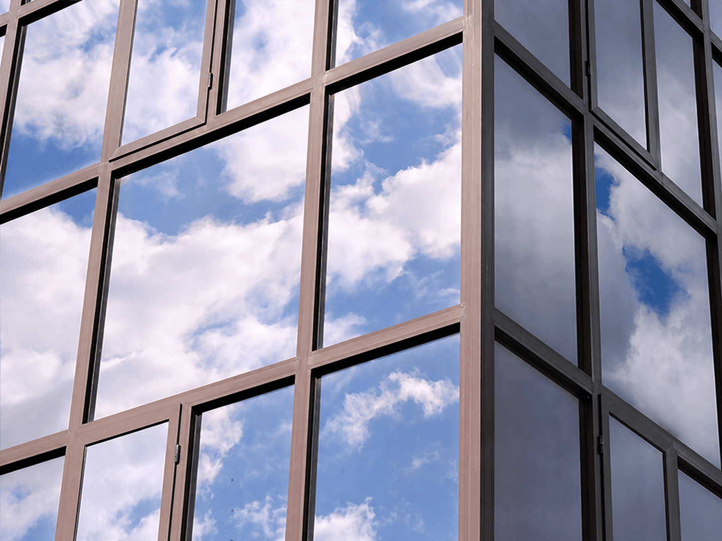 Glazen gevel met grote raamvlakken en reflectie van blauwe lucht met witte wolken, toegepast als opvallende architectonische glasafwerking.