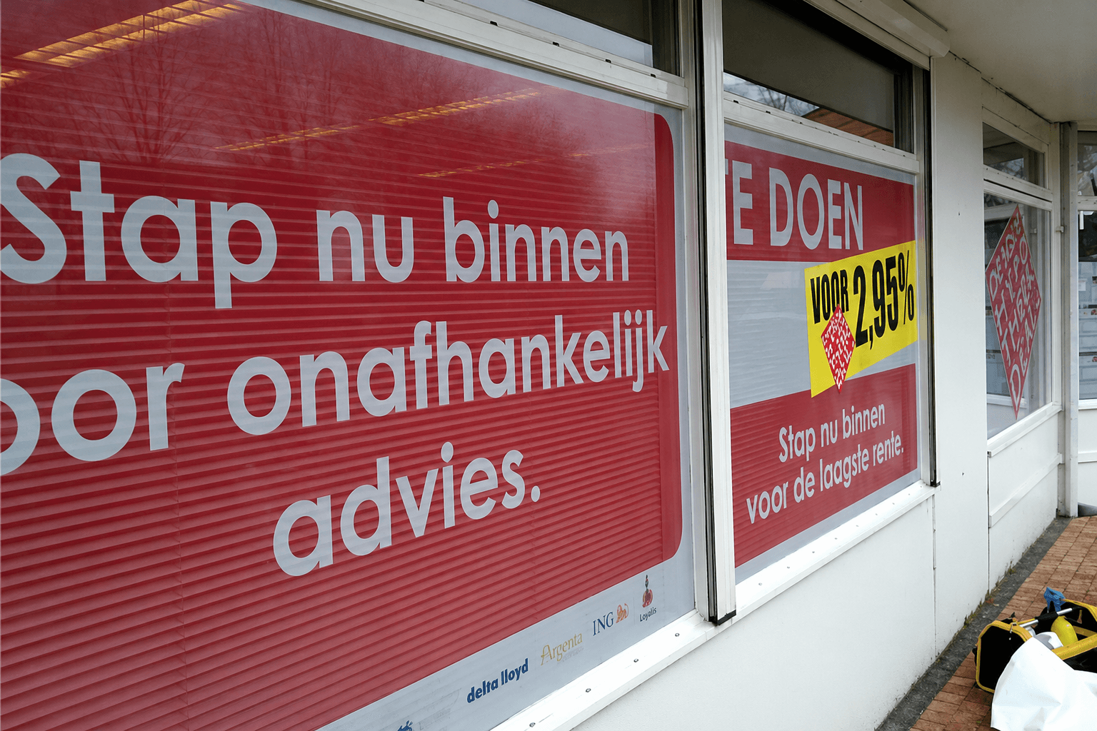 Rode raamstickers met witte promotietekst en gele actiesticker op de etalageramen van een winkelpand.