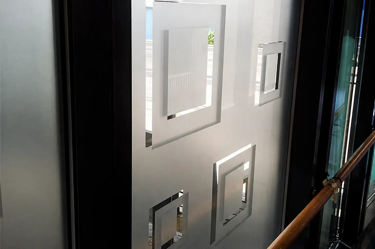 Matte glasfolie met geometrische vierkante uitsparingen op een glazen wand langs een trapleuning.