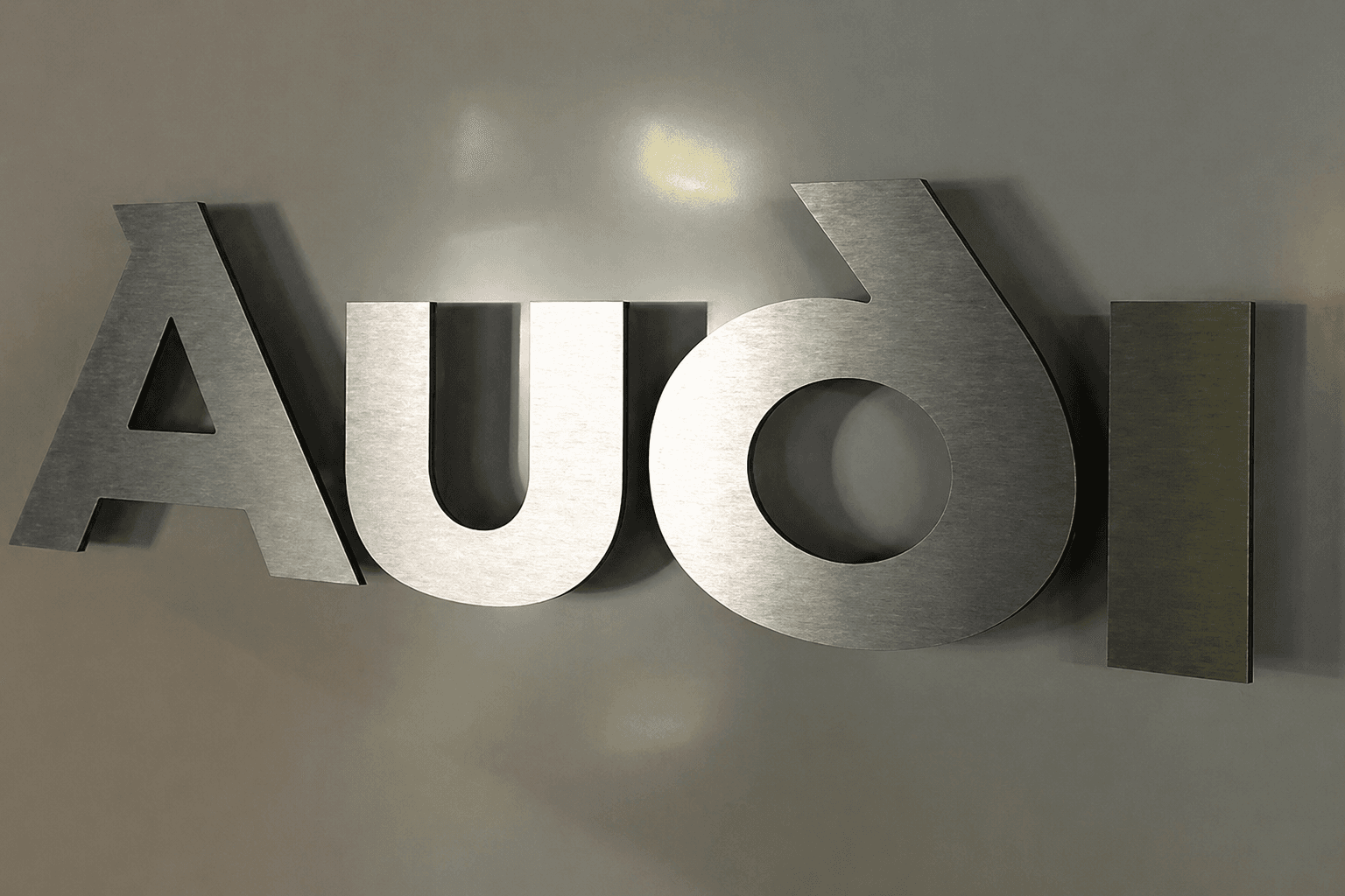 Metalen 3D wandletters met geborstelde afwerking, gemonteerd op afstandhouders tegen een grijze binnenmuur voor strakke bedrijfsreclame.