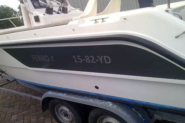 Witte motorboot op trailer met donkerblauw zijpaneel en grijze bootbelettering met naam en registratienummer 15-82-YD.