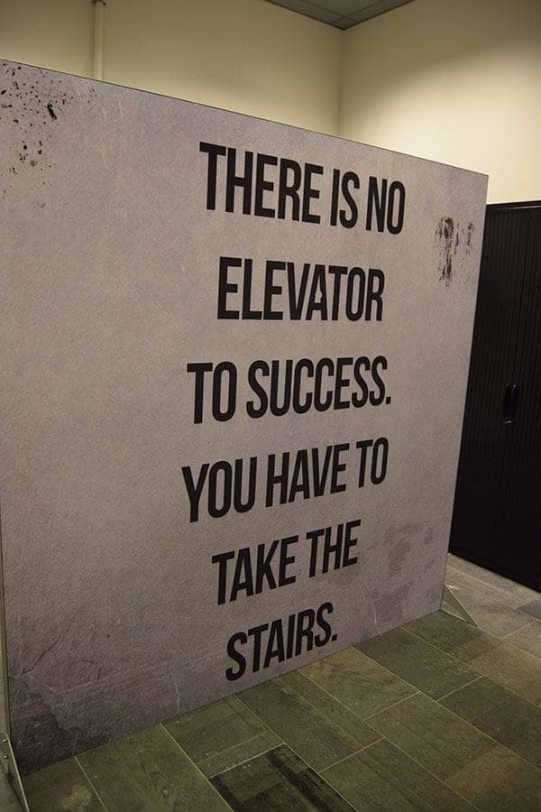 Vrijstaand grootformaat tekstpaneel met motiverende typografie “There is no elevator to success, you have to take the stairs” in een modern kantoorinterieur.