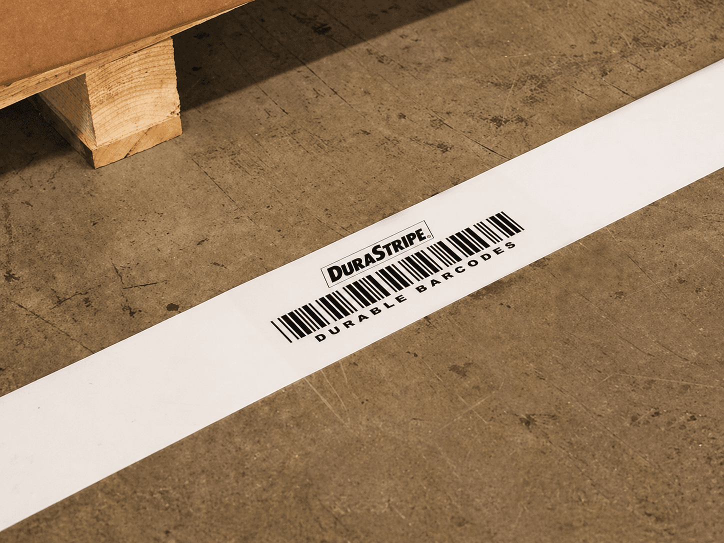Witte DuraStripe vloermarkering met barcode op een industriële betonvloer, toegepast als duurzame identificatiesticker voor logistiek en magazijnbeheer.