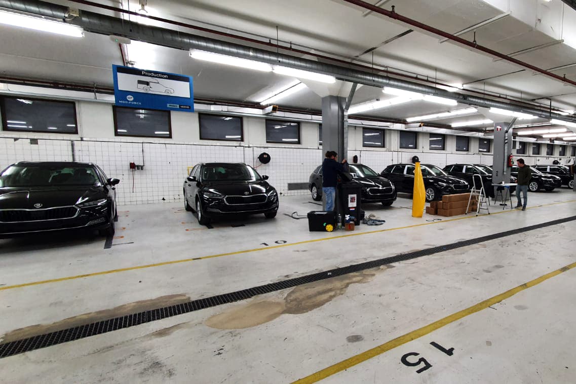 Werkplaats met meerdere zwarte auto’s in een productieruimte, waar monteurs bezig zijn met voertuigbelettering en voorbereiding van autoreclame.