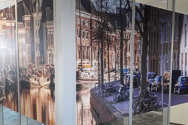 Glazen scheidingswand in kantoor met full-colour glasfolie van een stadsgezicht met grachtenpanden en fietsen, toegepast als decoratieve privacyfolie.