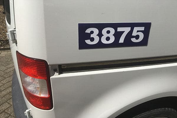 Een witte bestelwagen met een blauwe magneetplaat waarop het nummer 3875 staat.