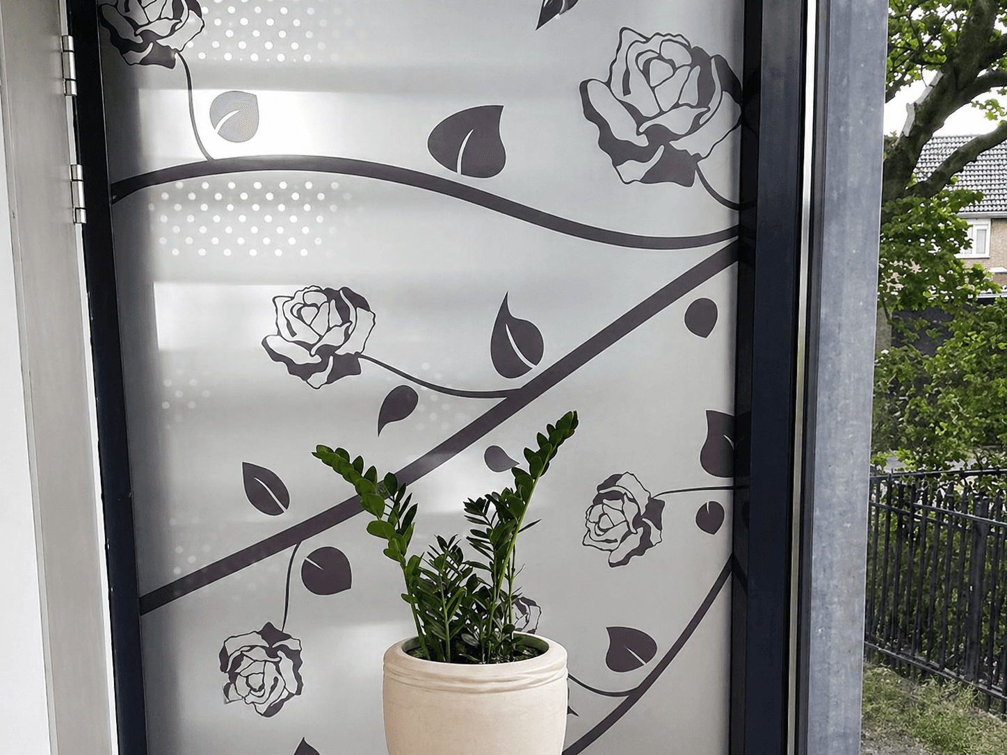 Matte glasfolie met bloem- en rankmotief op een raam, toegepast als decoratieve privacyfolie in een interieur met plantenbak.
