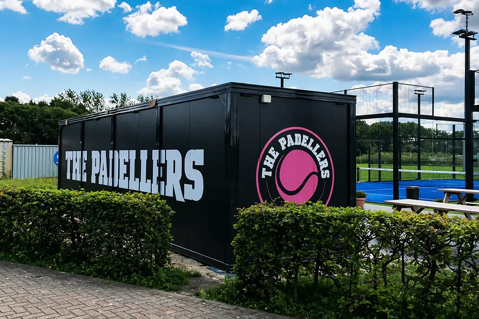 Zwarte containerunit met grote The Padellers-belettering en rond logo, geplaatst naast blauwe padelbanen als opvallende buitenreclame.