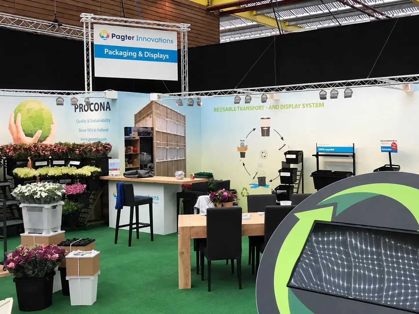 Beursstand van Pagter Innovations met groot trussbord, wandbelettering voor PROCONA en informatieve signing over herbruikbare transport- en displaysystemen tussen bloemenpresentaties.