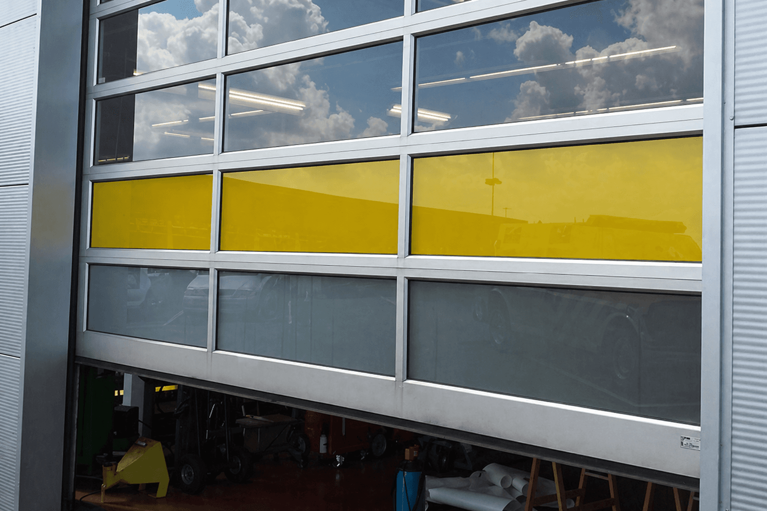 Gele en grijze raamfolie op aluminium glasdeuren van een bedrijfspand, toegepast als opvallende glasdecoratie en privacyfolie.