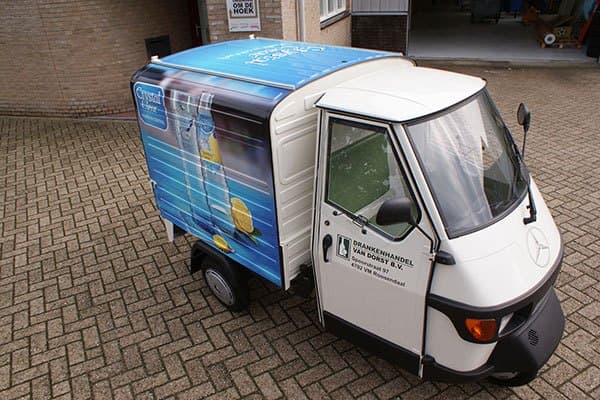 Compacte bezorgscooter met gesloten laadbak en full-color voertuigbelettering voor Crystal Clear, voorzien van productafbeeldingen op de zijpanelen en bedrijfslogo op het portier.