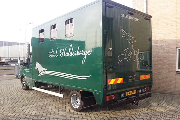Groene paardenvrachtwagen met Stal Halderberge-belettering, witte paardenafbeelding op de zijkant en Sporthorses-tekst op de achterdeuren, geparkeerd op een bedrijventerrein.
