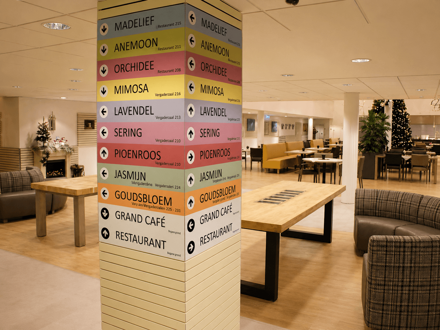 Kleurrijke wayfinding op een zuil met pijlen naar vergaderzalen, restaurant en grand café, toegepast als duidelijke binnenbewegwijzering in een horecaruimte.