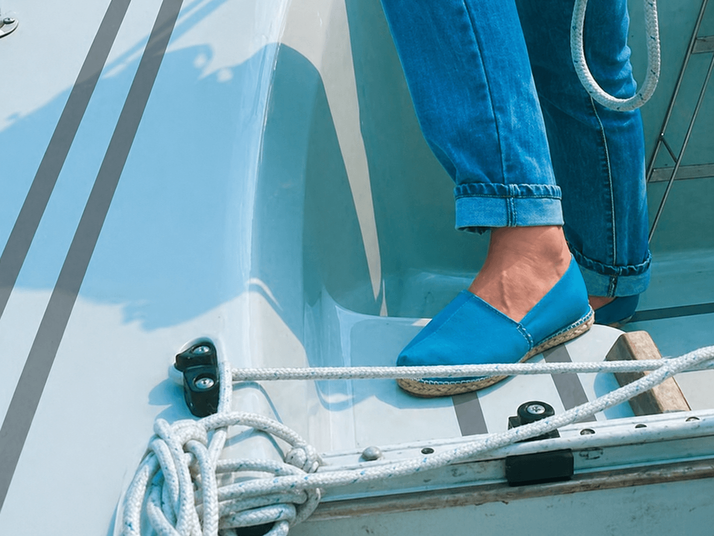 Grijze antislipstrips op een wit bootdek met touwen en een blauwe schoen, toegepast als subtiele veiligheidsmarkering voor grip aan boord.