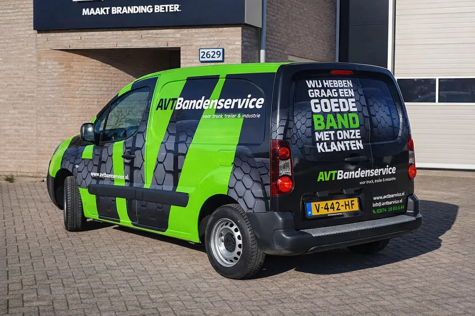 Groen-zwarte bestelwagen met opvallende voertuigbelettering van AVT Bandenservice, voorzien van grote witte tekst, felgroene banen en een bandenprofiel-graphic op de zijkant en achterdeuren, geparkeerd voor een bedrijfspand.