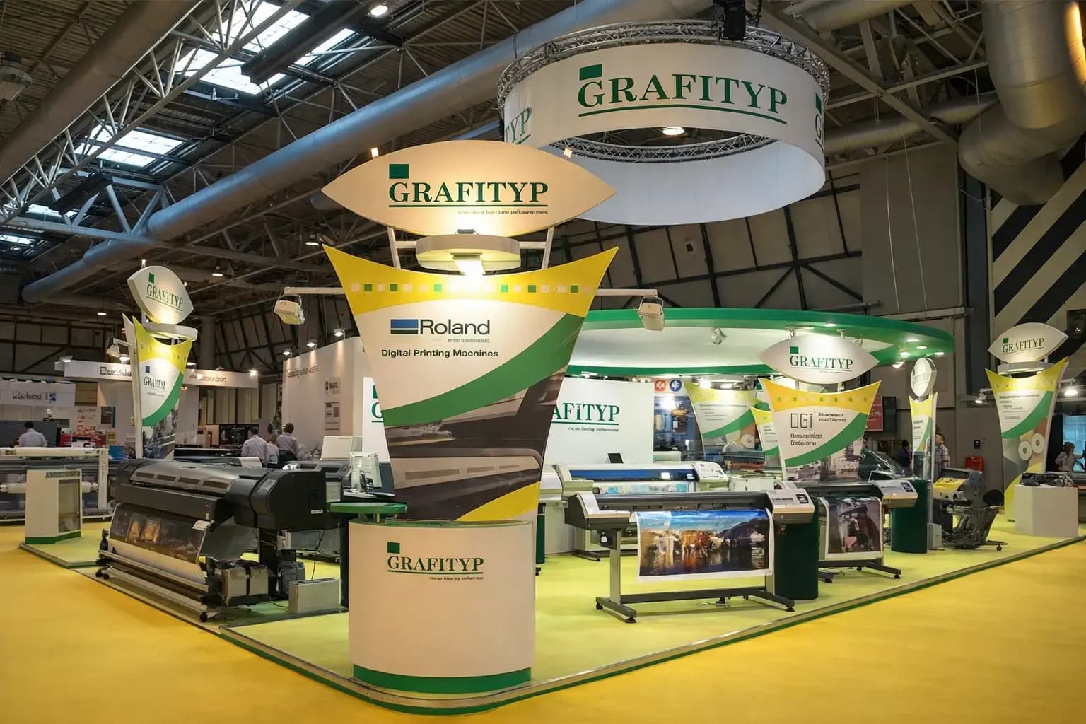 Ruime GRAFITYP-beursstand met hangende logobanner, hoge displayzuilen en grootformaat printers voor digitale printtoepassingen op een vakbeurs.
