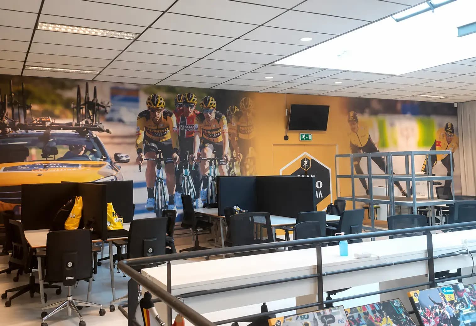 Kantoorruimte met kamerbrede wandprint van Team Jumbo-Visma wielrenners, toegepast als opvallende interieurvisual en decoratieve wandbekleding achter werkplekken.