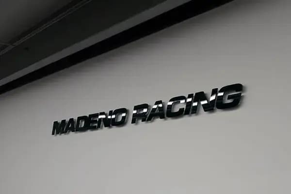 Witte binnenwand met glanzende zwarte 3D letters "MADENO RACING" als strakke interieurbelettering.