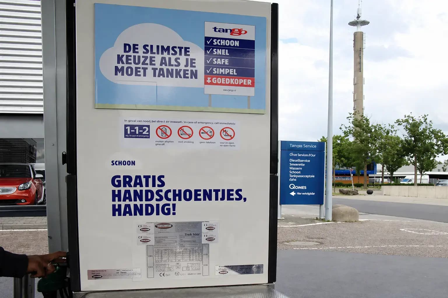 Informatieborden en veiligheidsstickers op een Tango-tankzuil, met promotiebord voor tanken en gratis handschoentjes bij een tankstation.