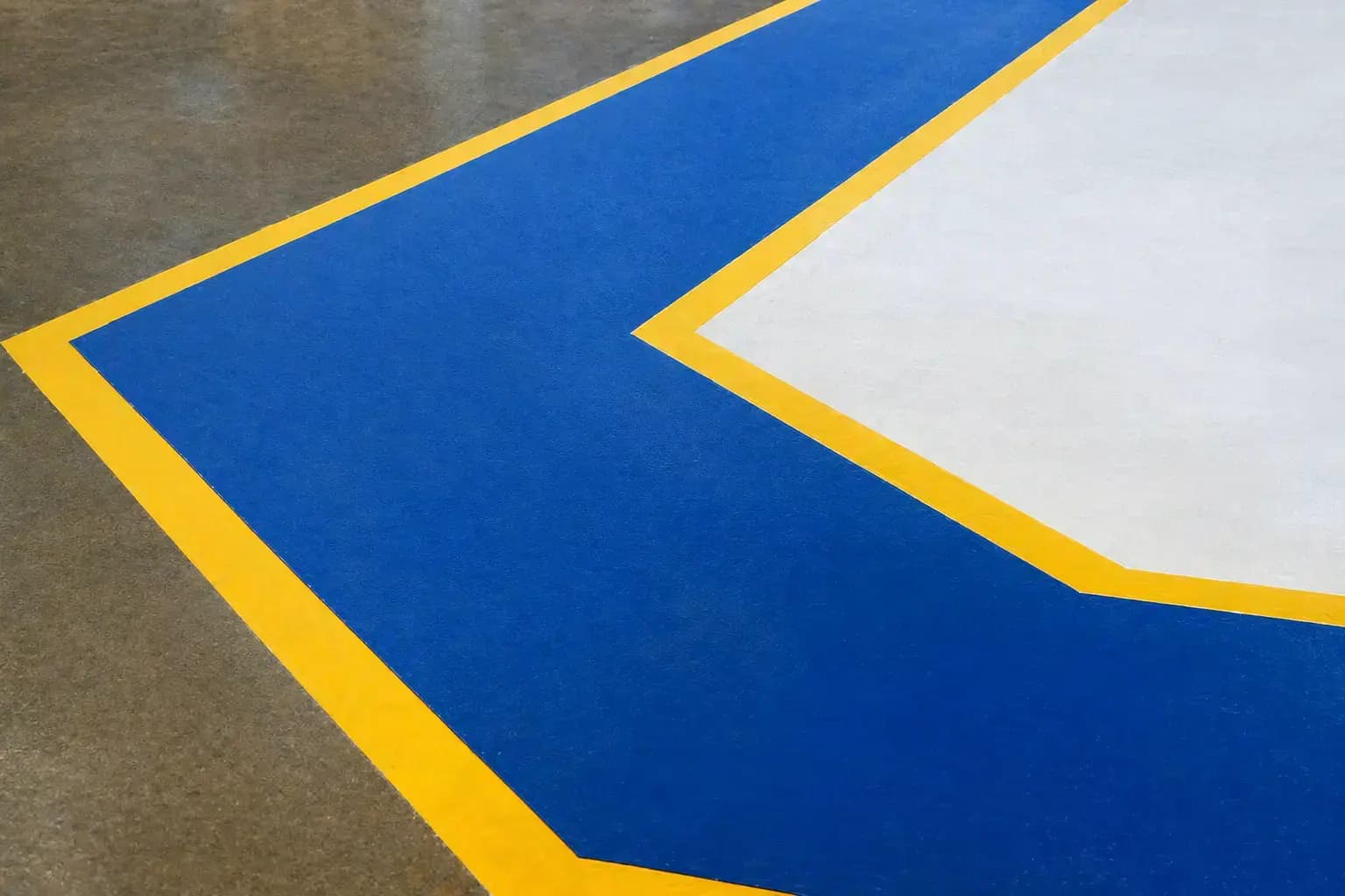 Blauwe vloerzone met gele belijning en witte markering op een industriële betonvloer, toegepast als duidelijke veiligheidsmarkering en routeaanduiding.
