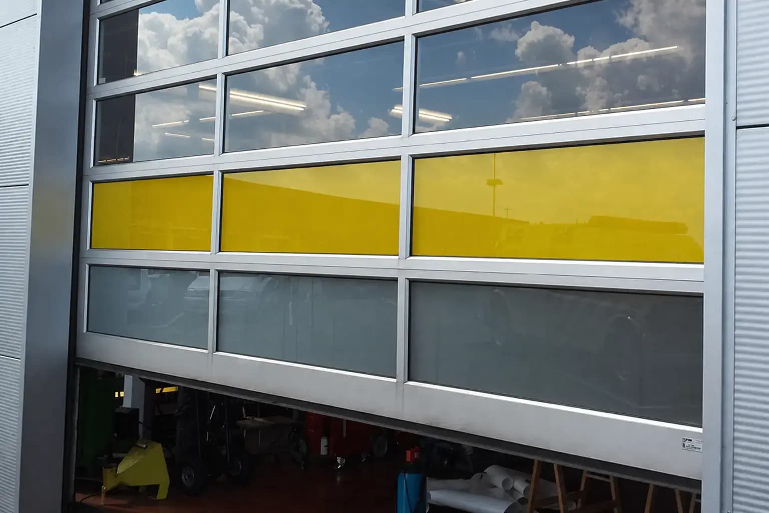 Gele en grijze raamfolie op aluminium glasdeuren van een bedrijfspand, toegepast als opvallende glasdecoratie en privacyfolie.