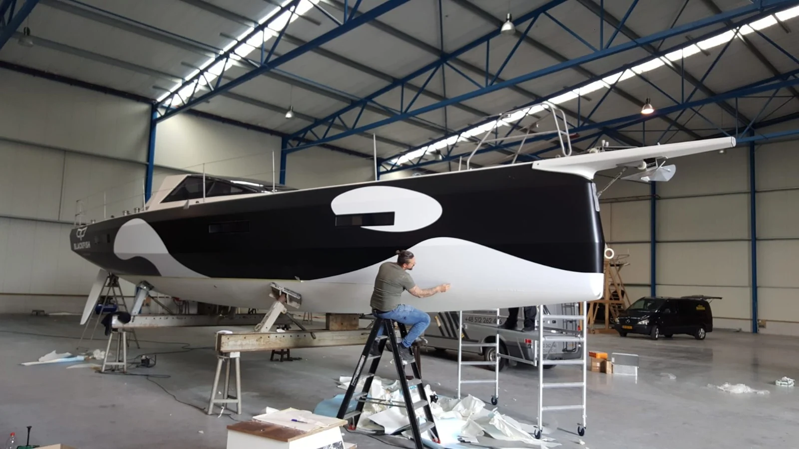 Fitting black and white hull graphics to a sailing boat in a hall.