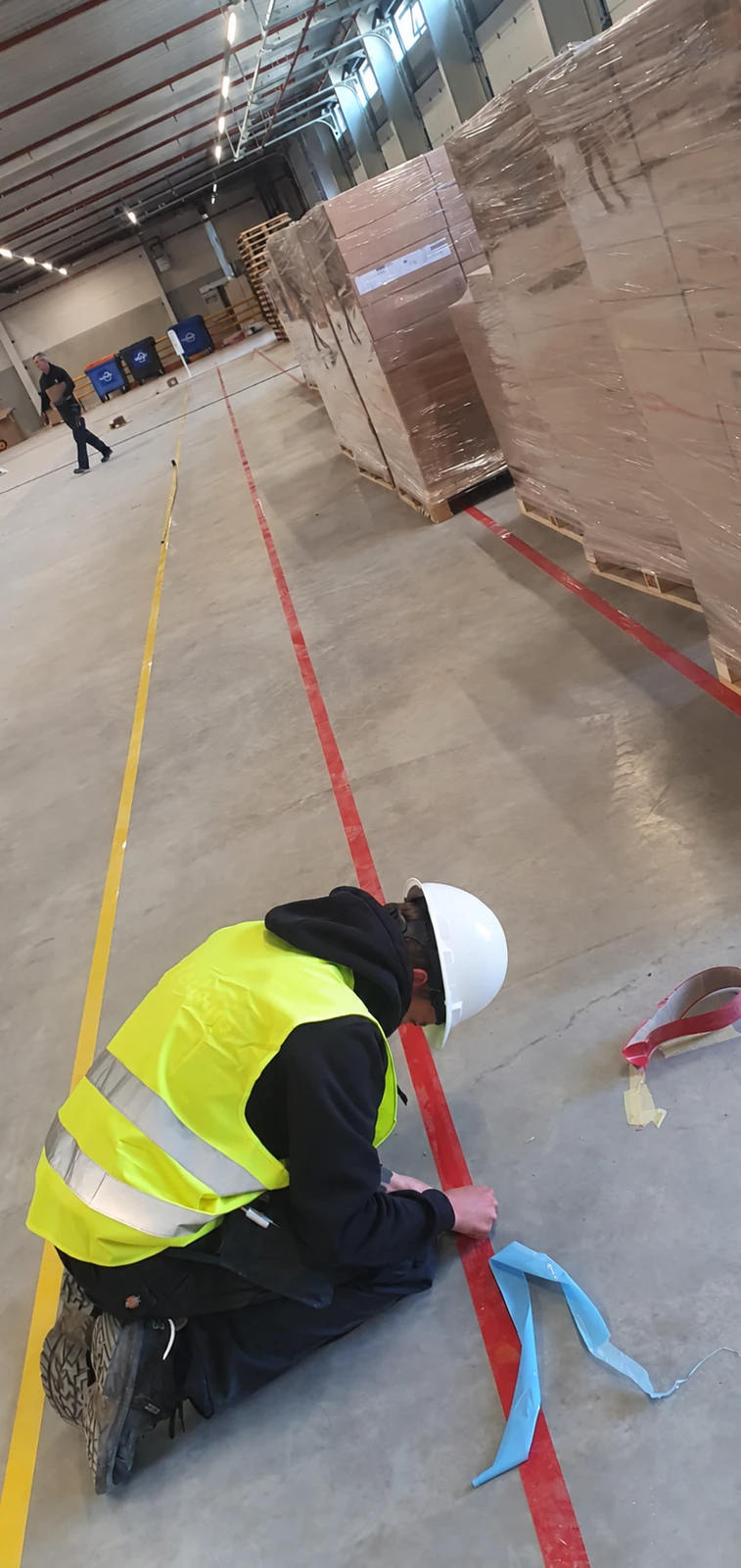 Installation of red floor tape beside a yellow line and stored pallets