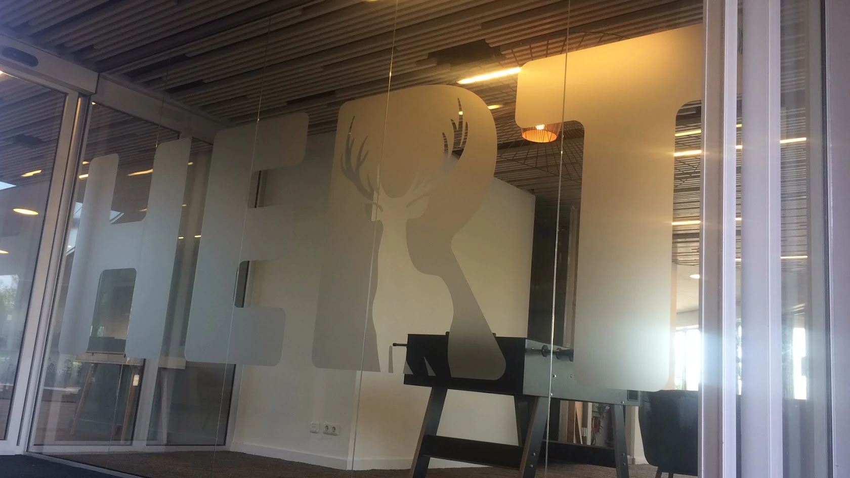 Large frosted HBT letters on clear glass, with a deer cut out within the logo