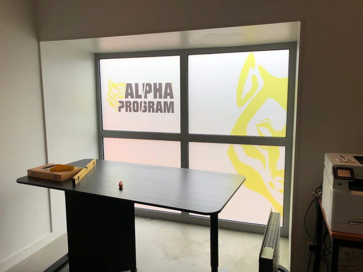 Printed window film with a yellow graphic and The Alpha Program branding