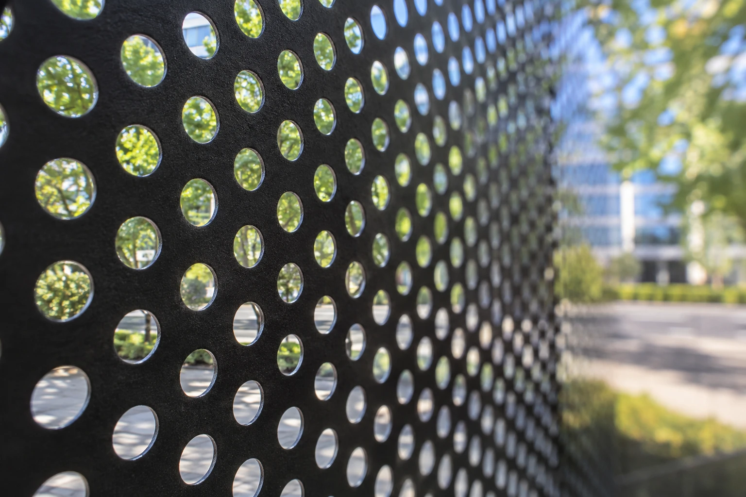 AI close-up from inside black One Way Vision film showing round open perforations and a view outdoors
