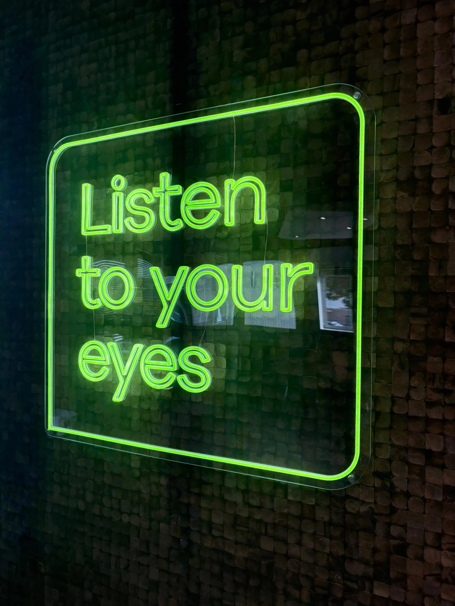Green neon-style Listen to your eyes lettering on a textured natural wall
