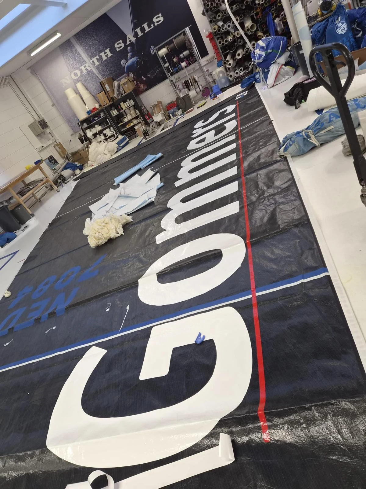 Large Gommers lettering being applied to a racing sail in a sail loft